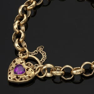 Puede incluir: Un brazalete de cadena de oro con un cierre de candado en forma de corazón. El candado tiene una piedra preciosa púrpura en el centro y diseños florales intrincados.
