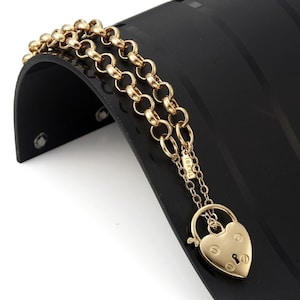 May include: A gold chain bracelet with a heart-shaped padlock charm. The charm has a keyhole and the words "18K GL" are engraved on the back.