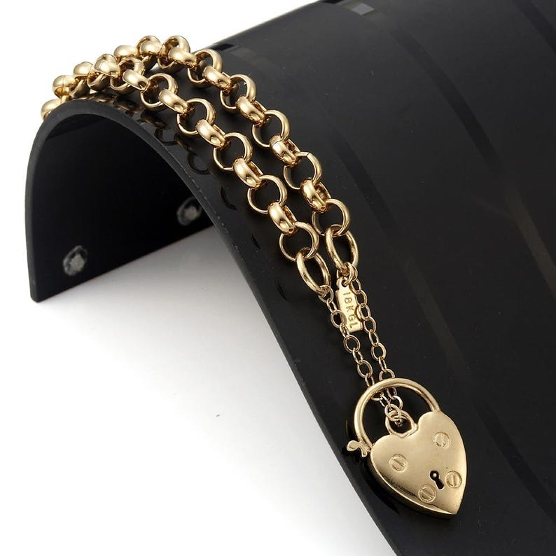 May include: A gold chain bracelet with a heart-shaped padlock charm. The charm has a keyhole and the words "18K GL" are engraved on the back.