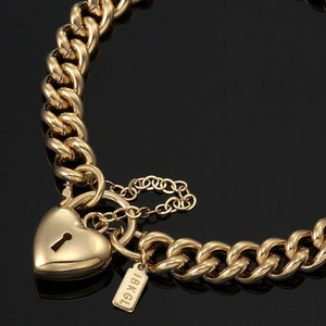 May include: A gold chain bracelet with a heart-shaped padlock clasp. The bracelet has a thick curb chain design and a small tag that reads "18KGL". The heart-shaped clasp has a keyhole detail.