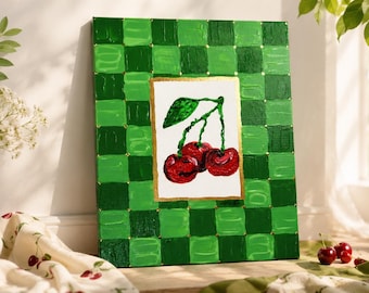 May include: A rectangular canvas painting featuring a central white panel with a textured red cherry illustration and green leaves, surrounded by a thick border of alternating light and dark green painted squares with gold accents.