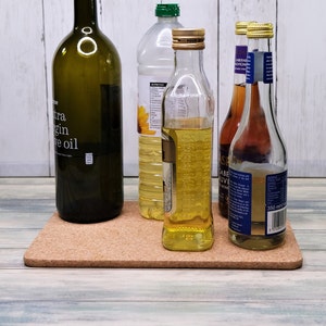 Op de afbeelding: Vier glazen flessen op een kurken onderzetter. De flessen bevatten olijfolie, zonnebloemolie en twee flessen rode wijnazijn. De flessen staan op een houten oppervlak.