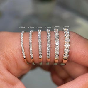 Puede incluir: Seis anillos de eternidad de oro engastados con pequeños diamantes redondos, ordenados por ancho de 1,00 mm a 2,50 mm. Cada anillo presenta una hilera de piedras brillantes, con las etiquetas 1,00 mm, 1,20 mm, 1,50 mm, 1,70 mm, 2,00 mm y 2,50 mm.