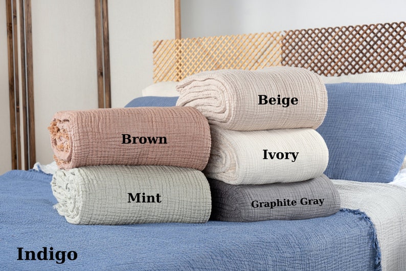 Puede incluir: Una pila de seis mantas de tejido de gofre de algod&oacute;n en varios colores, incluyendo &iacute;ndigo, gris grafito, menta, marfil, beige y marr&oacute;n. Las mantas est&aacute;n dobladas y apiladas en una cama.
