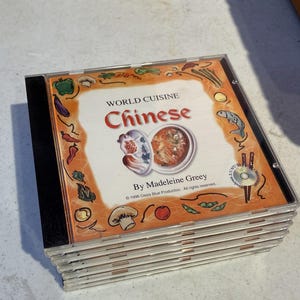 May include: A pile of CD-ROMs with the cover of "World Cuisine Chinese" by Madeleine Greey. The cover art features illustrations of Chinese food and ingredients, with the title in red and the author's name below.