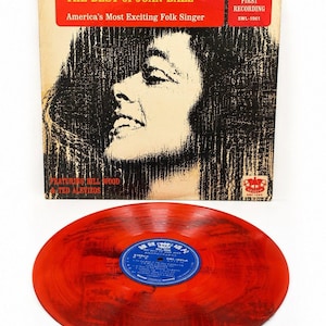 May include: A vintage vinyl record album featuring Joan Baez. The album cover has a red banner with the text "THE BEST of JOAN BAEZ" and "America's Most Exciting Folk Singer." The record is red with a blue label.
