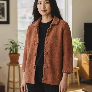 Puede incluir: Chaqueta abotonada de color óxido con tejido de punto texturizado. La chaqueta tiene cuello y mangas tres cuartos. Los bordes están adornados con una costura decorativa. La persona lleva una camisa negra y pantalones negros.