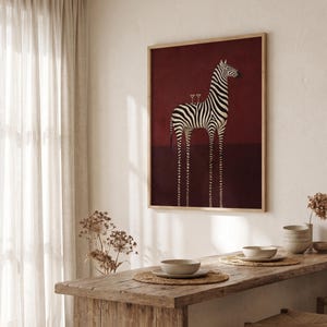 Pu&ograve; includere: Una stampa artistica incorniciata raffigurante una zebra stilizzata con zampe allungate su uno sfondo bordeaux intenso. La zebra presenta strisce bianche e nere e due piccoli bicchieri da martini sono in equilibrio sul dorso al centro.