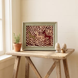 Puede incluir: Una impresi&oacute;n rectangular enmarcada que presenta tres figuras de jirafas estilizadas sobre un fondo de rayas de cebra en color marr&oacute;n oscuro y crema. El marco es de color verde claro con un acabado desgastado. Las jirafas tienen peque&ntilde;os patrones de estrellas.