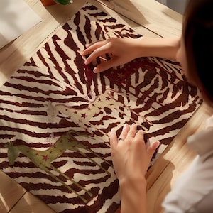 Puede incluir: Una hoja rectangular con un patr&oacute;n de rayas de cebra en marr&oacute;n y blanco como fondo. Tres ilustraciones estilizadas de jirafas se superponen a las rayas, cada una decorada con peque&ntilde;as estrellas rojas. Las jirafas son de color rojo, crema y verde.