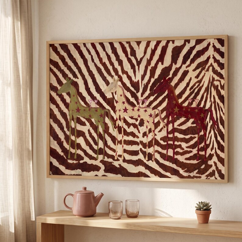 Puede incluir: Una pieza de arte mural rectangular enmarcada con un fondo de rayas de cebra marr&oacute;n y blanco, con tres figuras de caballos estilizadas en verde, crema y rojo oscuro, decoradas con estrellas y llevando un peque&ntilde;o vaso en el lomo.