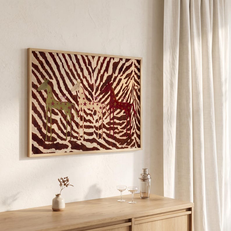 Puede incluir: Una pieza de arte mural rectangular en un marco de madera clara con un fondo de rayas de cebra en marr&oacute;n oscuro y crema, con tres figuras de jirafas estilizadas en verde, crema y rojo oscuro, decoradas con peque&ntilde;as estrellas.
