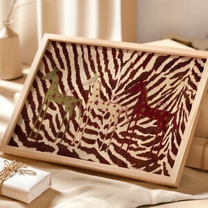 Puede incluir: Un marco de madera rectangular que contiene una impresi&oacute;n con un fondo de rayas de cebra en marr&oacute;n y blanco. Tres figuras de caballos estilizadas en verde, crema y rojo oscuro se sit&uacute;an en el centro, decoradas con peque&ntilde;os patrones de estrellas.