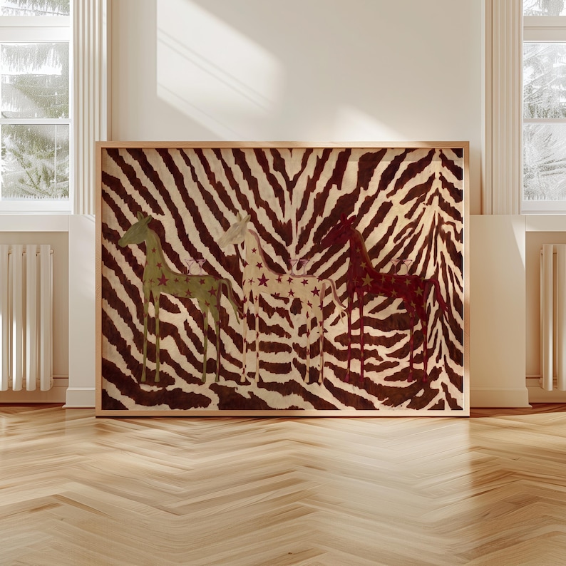Puede incluir: Una pieza de arte mural rectangular enmarcada que presenta un fondo de rayas de cebra en marr&oacute;n y blanco. Tres figuras de jirafas estilizadas est&aacute;n colocadas en fila, coloreadas en verde apagado, crema y rojo oscuro, decoradas con estrellas.