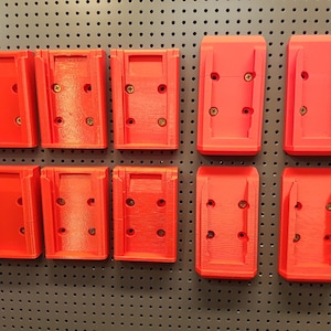 Puede incluir: Nueve soportes de pared de plástico rojo con agujeros para tornillos para colgar artículos en una placa perforada.