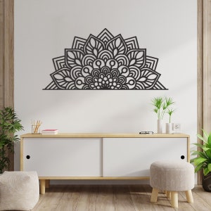 Op de afbeelding: Een zwart, halfrond mandala-wandkunstwerk. Het ontwerp bevat ingewikkelde bloemen- en geometrische patronen, waardoor een symmetrisch en decoratief element ontstaat. Het kunstwerk is gemonteerd op een witte muur boven een witte kast met houten accenten.