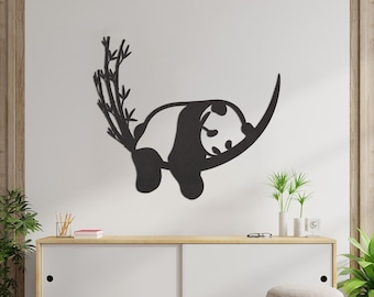 Puede incluir: Decoración de pared de metal negro con un oso panda colgado de una rama de bambú. El panda está en posición de dormir con la cabeza apoyada en la rama. La decoración está montada en una pared blanca sobre una cómoda de madera con un cajón blanco.