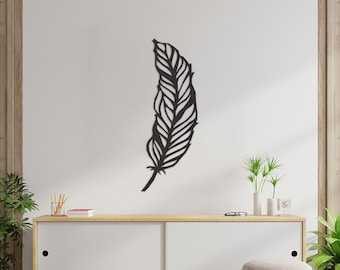 Puede incluir: Decoración de pared de metal negro en forma de una gran pluma. La pluma está montada en una pared blanca sobre una cómoda de madera con cajones blancos.