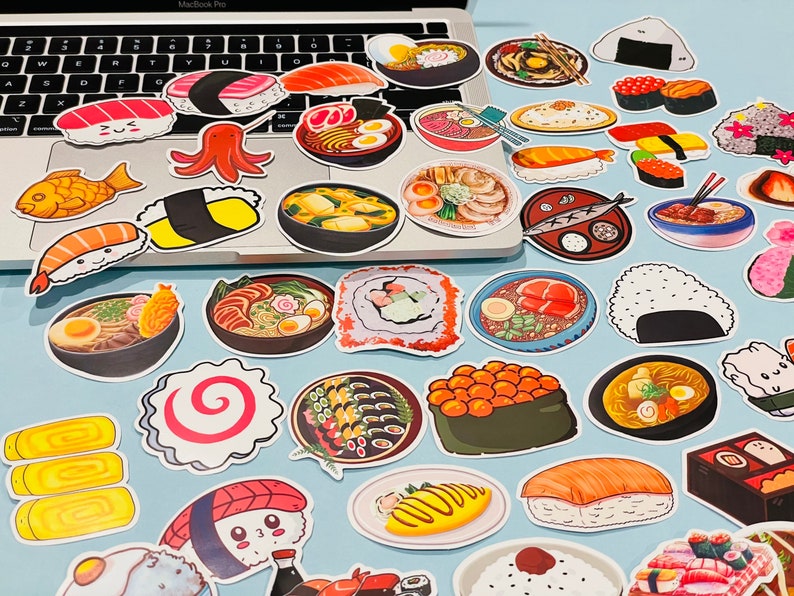 May include: A collection of colorful stickers featuring various Japanese food items, including sushi, ramen, and onigiri. The stickers are arranged in a grid pattern on a white surface.