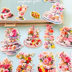 Puede incluir: Un conjunto de 10 pegatinas coloridas con arreglos florales, tazas de té y pasteles. Las pegatinas son perfectas para agregar un toque de fantasía a los planificadores, diarios y otros proyectos de manualidades.
