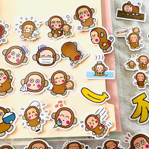 Puede incluir: Una colección de pegatinas con temática de monos, que representan monos de dibujos animados en varias poses y expresiones. Las pegatinas presentan monos marrones, algunos sosteniendo plátanos, usando máscaras o con notas musicales.