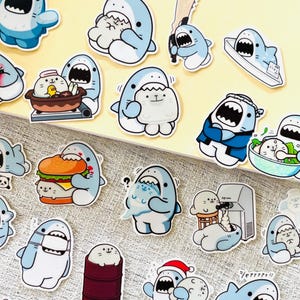 May include: A selection of cartoon shark stickers in different poses. The stickers depict sharks with open mouths, some interacting with food or other items. The color scheme includes blue, white, and red.
