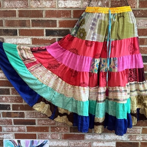 May include: A colorful patchwork skirt with a tiered design. The skirt features a variety of fabrics in shades of red, pink, green, and blue. It has a drawstring waist and a flowing, bohemian style.