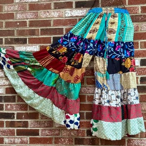 May include: Colorful patchwork pants with a wide leg design. The pants feature a variety of patterns and colors, including floral, paisley, and striped fabrics. The waistband is blue with a drawstring.