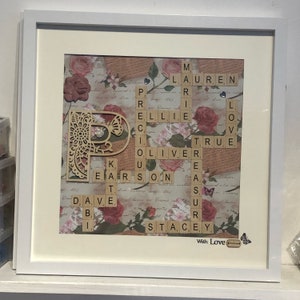 May include: A framed artwork featuring a decorative wooden letter "P" surrounded by a floral pattern. The letter is made up of Scrabble tiles spelling out names, including "Lauren", "Ellie", "Oliver", "True", "Stacey", and "Dave". The artwork also includes a small butterfly and the words "With Love".
