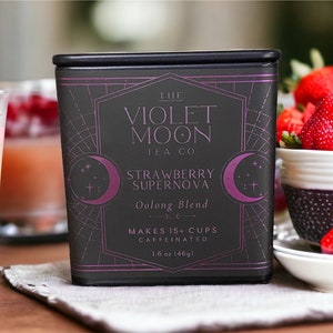 May include: A black tin of The Violet Moon Tea Co. Strawberry Supernova Oolong Blend tea. The tin has a purple crescent moon design with stars and a cross. The text on the tin reads "The Violet Moon Tea Co. Strawberry Supernova Oolong Blend. Makes 15+ cups. Caffeinated. 1.6 oz (46g)"