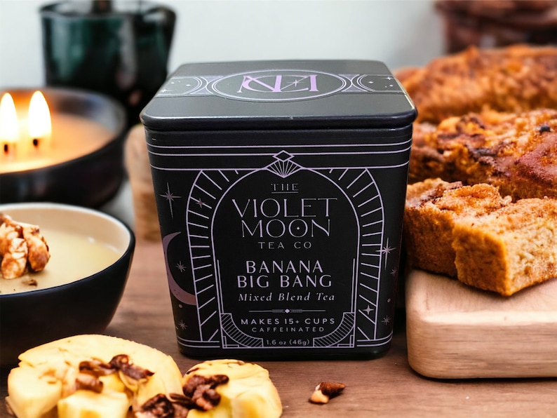 May include: A black tin container of loose leaf tea with a purple and white label. The label reads "The Violet Moon Tea Co. Banana Big Bang Mixed Blend Tea Makes 15+ Cups Caffeinated 1.6 oz (46g)"