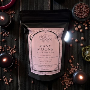 May include: A black pouch of "Many Moons" mixed blend tea from The Violet Moon Tea Co. The label is light pink with black text and includes the ingredients and brewing instructions. The pouch is 3.5 oz (99.2 g). The image includes candles and tea leaves.