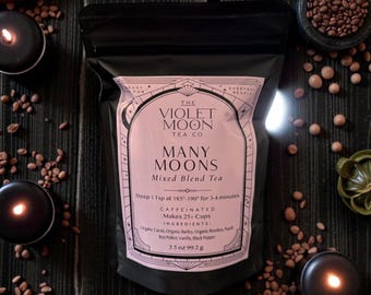 Puede incluir: Una bolsa negra de té de mezcla "Many Moons" de The Violet Moon Tea Co. La etiqueta es de color rosa claro con texto negro e incluye los ingredientes y las instrucciones de preparación. La bolsa es de 99,2 g. La imagen incluye velas y hojas de té.