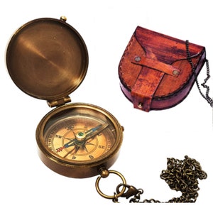 K&ouml;nnte beinhalten: Ein Kompass aus Messing mit einem Lederetui und einer Kette. Der Kompass hat ein klares Zifferblatt mit einer Kompassrose und einer Nadel. Das Etui ist braun und hat eine Klappe, die mit einem Druckknopf geschlossen wird.