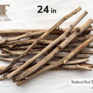 May include: A pile of weathered wood sticks, approximately 24 inches long, with a natural, light brown color. The sticks vary in thickness and have visible knots and textures. The image includes the text "Weathered Wood Sticks" and the brand name "Fairie Gifts".