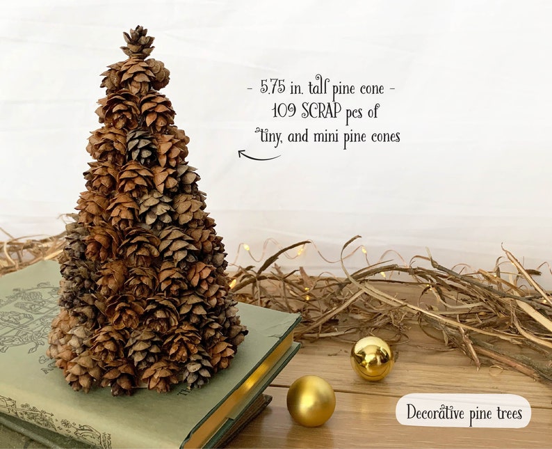 May include: A decorative pine cone tree, approximately 5.75 inches tall, crafted from 109 tiny and mini pine cones. The tree is brown and sits on a book. Two gold ornaments are nearby. The text reads "Decorative pine trees".