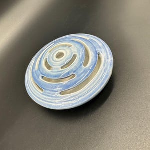 Puede incluir: Un portaincienso ovalado de cerámica con un diseño en espiral. El soporte está pintado en tonos azules y blancos, con cortes curvos. Este artículo decorativo es adecuado para la decoración del hogar.