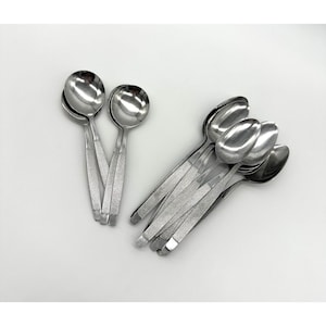 Puede incluir: Un conjunto de cucharas de acero inoxidable con una superficie brillante y reflectante. Las cucharas tienen un diseño sencillo y elegante con un mango texturizado. La imagen muestra varias cucharas agrupadas, lo que sugiere un juego de cubiertos.