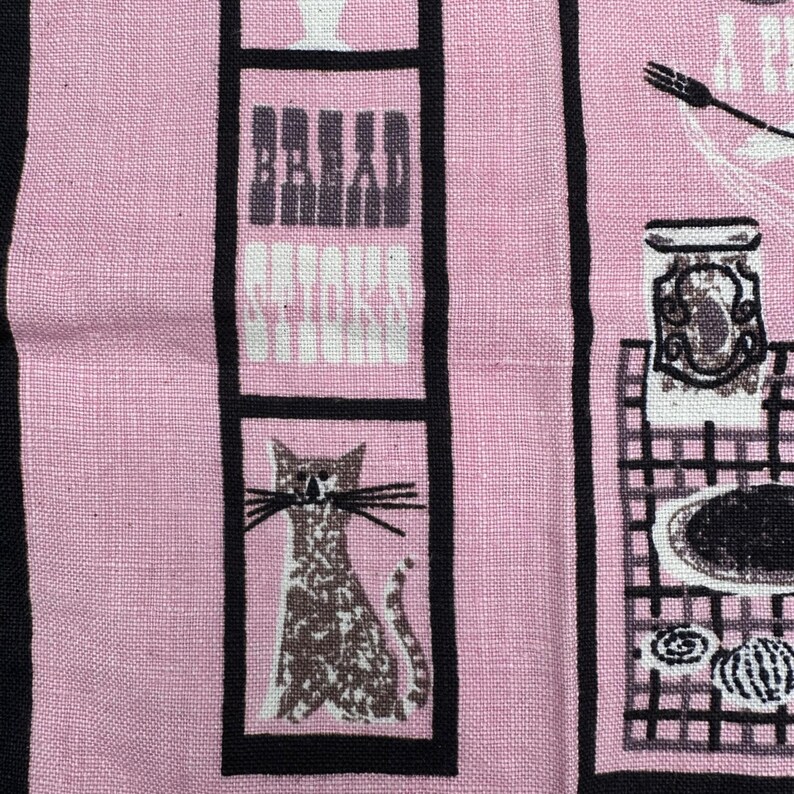 Pu&ograve; includere: Tessuto rosa con strisce verticali nere e illustrazioni incorniciate. Il tessuto presenta un gatto, il testo "Bread Sticks" e disegni a tema cucina. Il design generale ha un'estetica vintage.