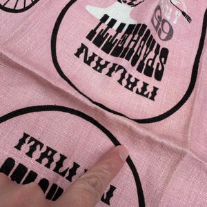 Pu&ograve; includere: Tessuto rosa con disegni circolari neri. Ogni cerchio contiene le parole "Italian Spaghetti" e una grafica di una tastiera di pianoforte. Il tessuto ha una consistenza leggermente stropicciata.