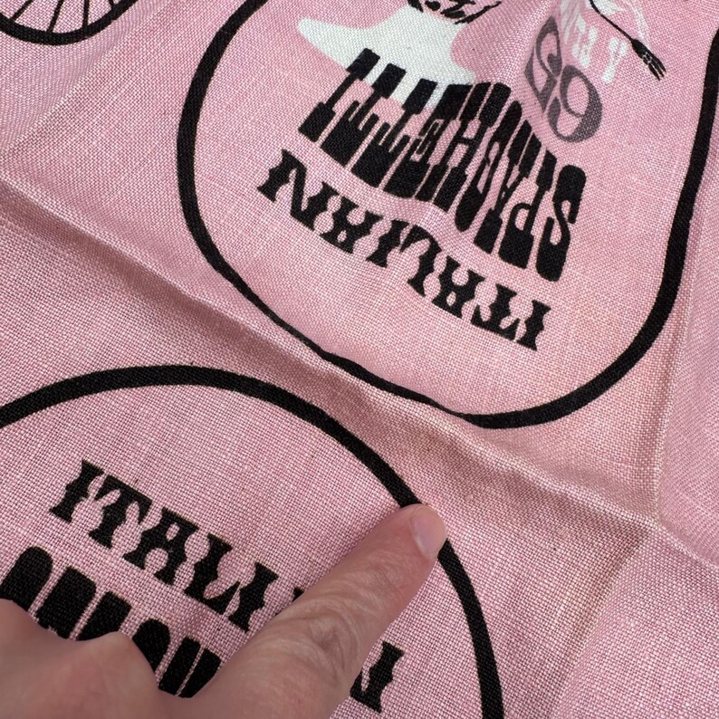 Pu&ograve; includere: Tessuto rosa con disegni circolari neri. Ogni cerchio contiene le parole "Italian Spaghetti" e una grafica di una tastiera di pianoforte. Il tessuto ha una consistenza leggermente stropicciata.