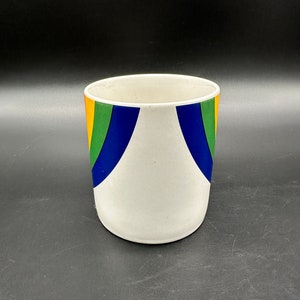 May include: White ceramic planter with a rainbow design. The planter has a wide mouth and a rounded bottom. The rainbow design is made up of orange, yellow, green, blue, and purple stripes.