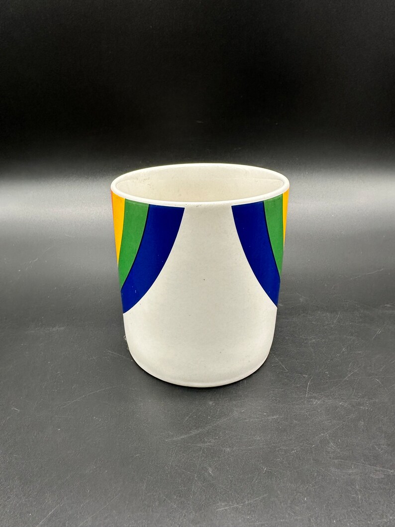 May include: White ceramic planter with a rainbow design. The planter has a wide mouth and a rounded bottom. The rainbow design is made up of orange, yellow, green, blue, and purple stripes.