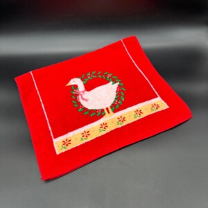 May include: Red hand towel with a white goose in a green wreath with a yellow and white border.