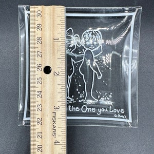 May include: A clear glass ashtray with a white border and a white illustration of two children holding hands. The text "the One you Love" is printed below the illustration. The text "Monty's" is printed in the bottom right corner.