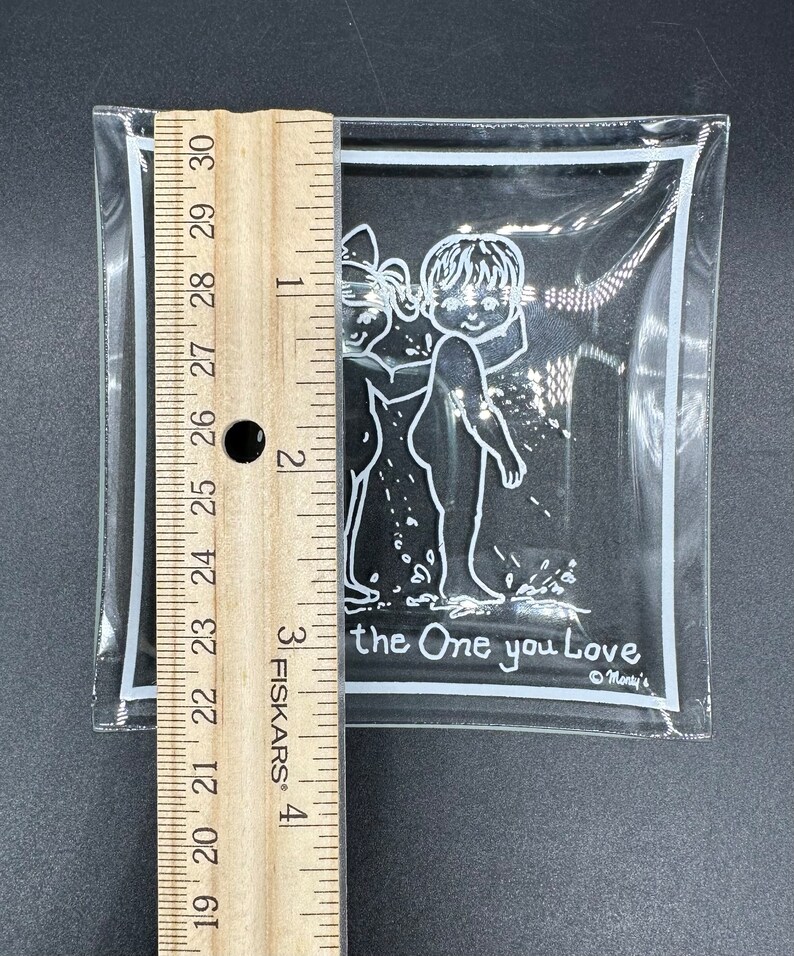 May include: A clear glass ashtray with a white border and a white illustration of two children holding hands. The text "the One you Love" is printed below the illustration. The text "Monty's" is printed in the bottom right corner.