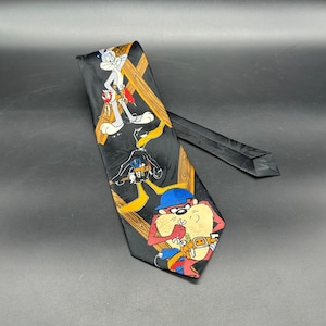 May include: Black necktie featuring cartoon characters Bugs Bunny, Daffy Duck, and Taz the Tasmanian Devil. The tie has a repeating pattern of the characters with wooden beams as a background.