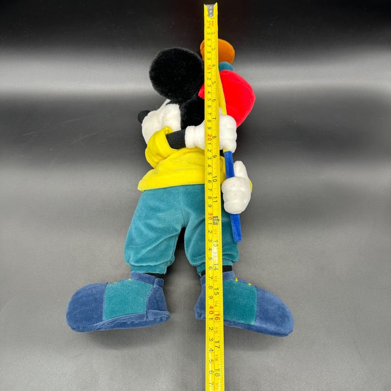 Puede incluir: Un juguete de peluche de Mickey Mouse con una camisa amarilla, pantalones azules y zapatos azules. Est&aacute; sosteniendo un palo de golf azul y amarillo y mide aproximadamente 46 cm de alto.