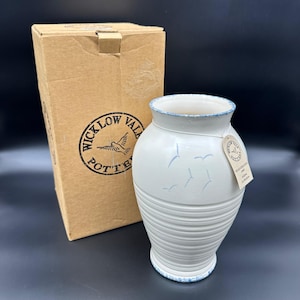 May include: White ceramic vase with a blue rim and a blue bird design. The vase is in a brown cardboard box with a label that says "Wicklow Valley Pottery".