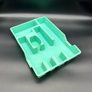 以下が含まれることがあります： 複数のサイズで異なる区画を持つ、薄い緑色のプラスチック製のトレイ。トレイは、さまざまなアイテムを収納および整理するために設計されています。